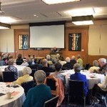 A man behind a podium gestures to a group of seated people